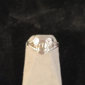 Puede incluir: Un anillo de tono plateado que presenta un icono central con forma de cabeza y dos orejas redondeadas. La banda del anillo se divide en dos segmentos met&aacute;licos finos y pulidos que se conectan a los lados del dise&ntilde;o central inspirado en un personaje.