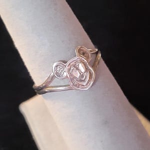 Puede incluir: Un anillo de metal plateado que presenta un dise&ntilde;o central recortado de una cabeza de rat&oacute;n de dibujos animados con dos orejas redondeadas. La banda es delgada y lisa, conect&aacute;ndose a la base del motivo de la cabeza del rat&oacute;n.