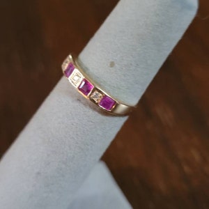 May include: A gold band ring with pink and white gemstones. The ring is on a white ring display stand.