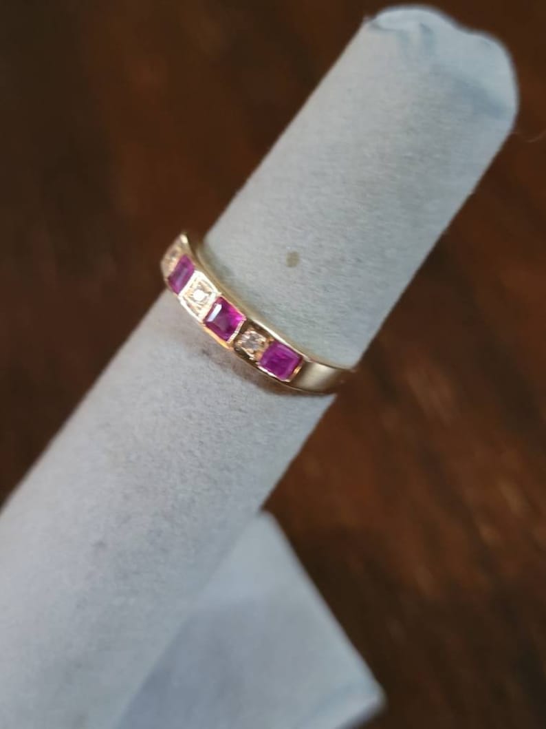 May include: A gold band ring with pink and white gemstones. The ring is on a white ring display stand.