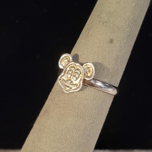 Pu&ograve; includere: Un anello in metallo color argento con un emblema in rilievo che raffigura la testa di Topolino sulla parte anteriore. La fascia &egrave; liscia e lucida, mentre il volto del personaggio presenta dettagli incisi con una finitura metallica uniforme.