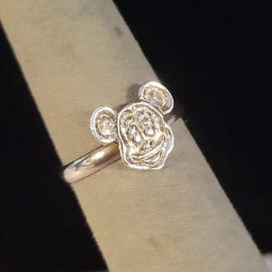 Pu&ograve; includere: Un anello in metallo color argento caratterizzato da un design a testa di personaggio in rilievo e testurizzato con due orecchie arrotondate. Il gambo dell'anello &egrave; liscio e lucido, con una finitura metallica che riflette la luce sulla superficie.