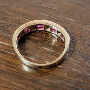 May include: A gold band ring with a row of pink square-shaped gemstones.