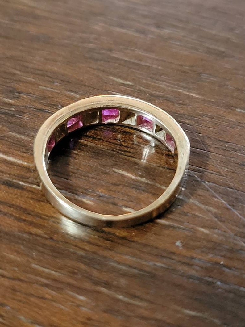 May include: A gold band ring with a row of pink square-shaped gemstones.