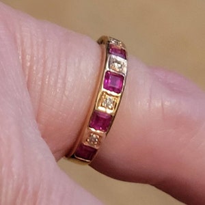 May include: A gold band ring with a row of square-shaped ruby stones and smaller diamond accents.