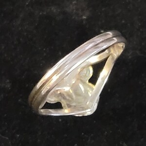 Puede incluir: Un anillo de metal plateado con un dise&ntilde;o de v&aacute;stago dividido que converge en la parte frontal. La banda tiene un acabado liso y pulido con una silueta en forma de V, con un espacio central abierto entre las dos bandas que se unen en un punto.
