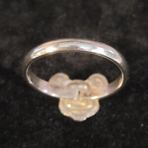 Pu&ograve; includere: Un anello color argento lucido caratterizzato da un prominente ornamento centrale a forma di fiore o trifoglio a tre petali. La fascia &egrave; liscia e arrotondata, con una finitura metallica riflettente che cattura la luce sulla superficie curva.