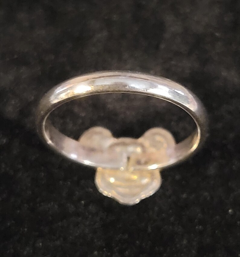 Pu&ograve; includere: Un anello color argento lucido caratterizzato da un prominente ornamento centrale a forma di fiore o trifoglio a tre petali. La fascia &egrave; liscia e arrotondata, con una finitura metallica riflettente che cattura la luce sulla superficie curva.