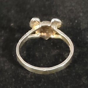 Puede incluir: Un anillo plateado con un peque&ntilde;o dise&ntilde;o en forma de oso de color dorado. El anillo tiene una banda simple y una cabeza de oso detallada con peque&ntilde;as orejas. El anillo est&aacute; sobre un fondo oscuro.