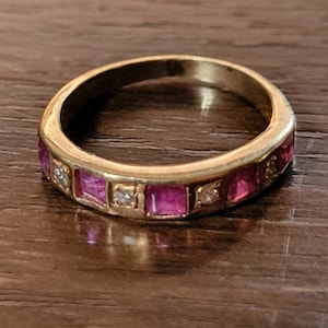 May include: A gold band ring with pink and clear square-shaped stones set in the band.