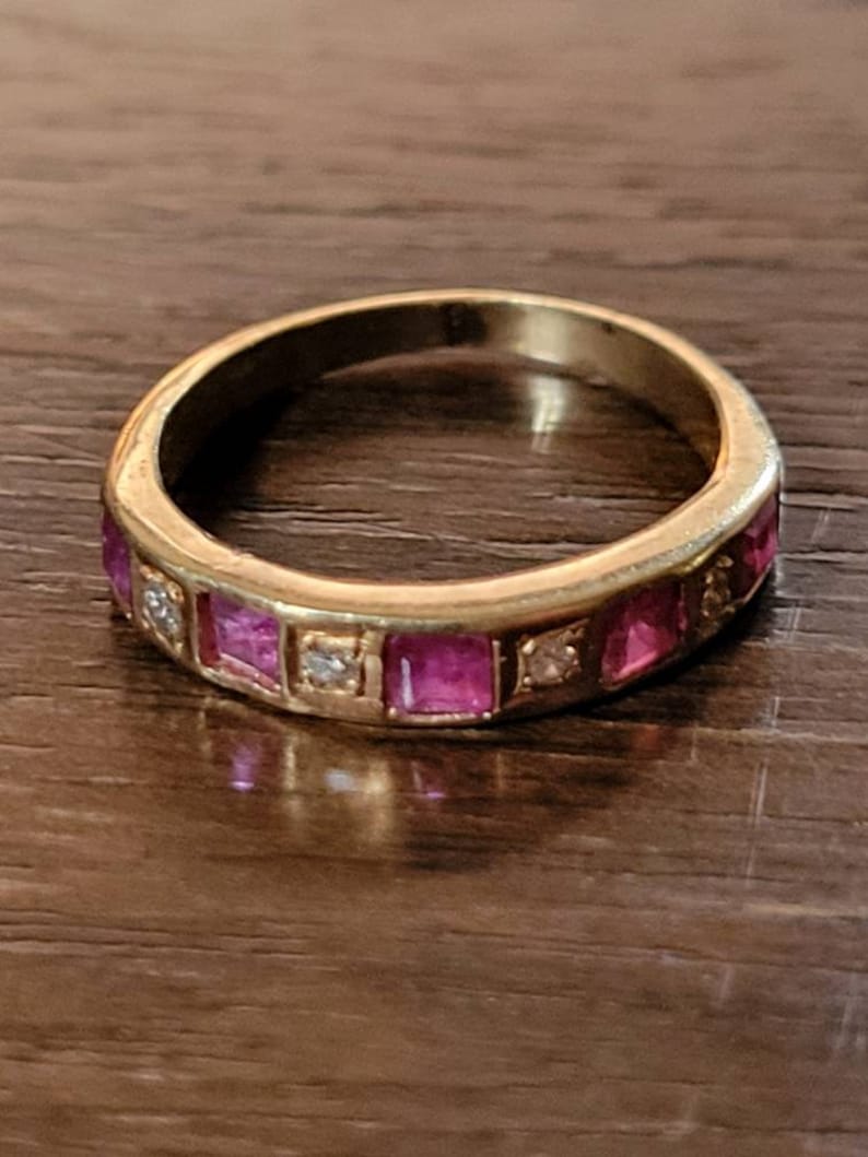 May include: A gold band ring with pink and clear square-shaped stones set in the band.