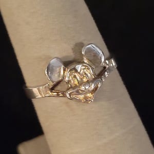 Puede incluir: Un anillo plateado con un dise&ntilde;o detallado de Mickey Mouse. El anillo muestra la cara y las orejas del personaje, con un acabado pulido. El anillo se muestra en un dedo, destacando su tama&ntilde;o y forma.
