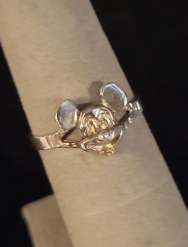 Puede incluir: Un anillo plateado con un dise&ntilde;o detallado de Mickey Mouse. El anillo muestra la cara y las orejas del personaje, con un acabado pulido. El anillo se muestra en un dedo, destacando su tama&ntilde;o y forma.
