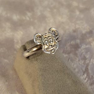 Pu&ograve; includere: Un anello in metallo color argento con la testa scolpita di un topo dei cartoni animati con grandi orecchie arrotondate. Il gambo dell'anello &egrave; liscio e circolare, mentre il volto del topo presenta dettagli in rilievo come occhi e naso.