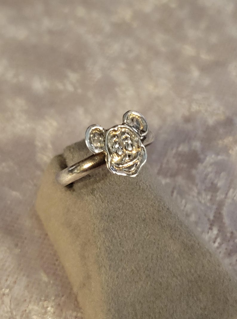 Pu&ograve; includere: Un anello in metallo color argento con la testa scolpita di un topo dei cartoni animati con grandi orecchie arrotondate. Il gambo dell'anello &egrave; liscio e circolare, mentre il volto del topo presenta dettagli in rilievo come occhi e naso.