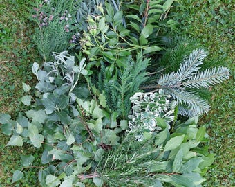 Könnte beinhalten: Eine Sammlung verschiedener frischer Grünpflanzen, darunter dunkelgrüne Nadelbaumzweige, silbriger Eukalyptus, panaschierte Blätter mit weißen Rändern, Rosmarinzweige, Lorbeerblätter und Stängel mit kleinen Beeren, angeordnet in einem dichten Bündel.