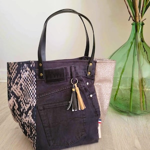 Peut inclure: Un sac cabas en denim noir avec un motif peau de serpent d'un côté et un tissu pailleté doré de l'autre. Le sac a des anses en cuir noir et un pompon doré.