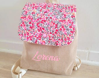 Op de afbeelding: Een beige corduroy rugzak met een roze bloemenstofklep en de naam "Lorena" geborduurd op de voorkant.