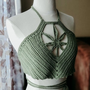 Pode incluir: Um top halter de crochê verde com um design de folha na frente. O top tem um laço nas costas e um laço na cintura.
