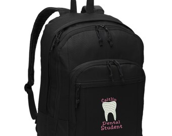 May include: A black backpack featuring a white embroidered tooth graphic and the pink embroidered text "Caitlin Dental Student". The bag includes a large main compartment, a smaller front pocket, and two black zipper pulls on each of the two sections.