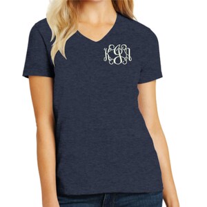 May include: A navy blue heathered V-neck t-shirt featuring a white embroidered monogram on the left chest. The monogram consists of the letters K, J, and A in a decorative, swirling script font, positioned clearly on the upper chest area.