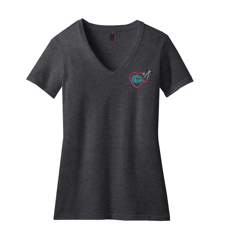 May include: A charcoal gray V-neck t-shirt featuring a small embroidered design on the left chest. The graphic consists of a pink heart outline, a teal brain illustration inside the heart, and a stethoscope extending from the heart shape.