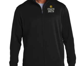 May include: A black full-zip jacket with a mock neck collar. On the upper left chest, there is a yellow basketball graphic above the white text "COACH SMITH" in a bold, block-style font. The jacket features long sleeves and a central zipper.