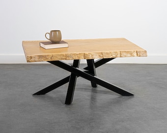 May include: A wooden coffee table with a live edge top and black metal X-shaped legs. A book and a brown ceramic mug are on the table.