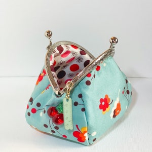 May include: A teal blue coin purse with a floral pattern and red cherries. The purse has a silver clasp and a small ruler charm.