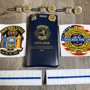 May include: A collection of New York State Correctional Officers & Police Benevolent Association items. Includes pins, stickers, and a blue booklet with the text "2025-2026". The stickers feature text such as "ROGUE" and "I WALKED THE LINE".