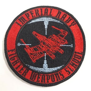 Puede incluir: Un parche bordado rojo y negro con las palabras "Imperial Navy Fighter Weapons School" en un círculo alrededor de un avión de combate rojo.