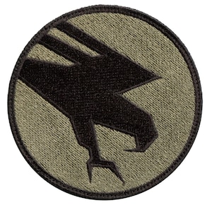 May include: A round, olive green patch with a black embroidered silhouette of a bird of prey with its talons extended.
