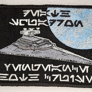 May include: A black embroidered patch with a white outline featuring a Star Destroyer spaceship against a blue planet background. The text "STAR DESTROYER" is written in white above the spaceship and "DEATH STAR" is written in white below the spaceship.