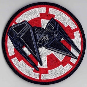 Puede incluir: Un parche bordado en blanco y negro con una silueta de caza TIE contra un símbolo imperial rojo y blanco.