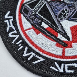 May include: Black and white embroidered patch with a red and white circle in the center. The circle features a stylized image of a spaceship. The text "VICTORY" is embroidered around the outside of the circle.