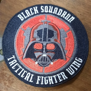 Peut inclure: Écusson brodé Black Squadron Tactical Fighter Wing avec un motif de Dark Vador en noir, gris et orange.