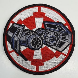 May include: A round embroidered patch featuring a TIE fighter in front of the Imperial symbol. The TIE fighter is gray and blue, and the symbol is red and white.