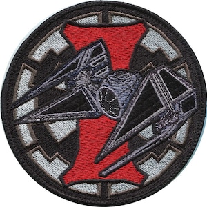 May include: A black and gray embroidered patch with a TIE fighter silhouette in the center. The TIE fighter is superimposed over a red 'I' and a black and gray Imperial symbol.