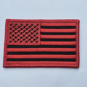 May include: Red embroidered American flag patch with black stitching. The patch is rectangular and has a white background with red stripes and a blue field of stars.