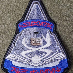 Puede incluir: Un parche bordado gris y blanco con un diseño de nave espacial. El parche tiene una cinta azul con el texto "HEAVY METAL" en letras rojas y una cinta azul con el texto "LIVE TO SURVIVE" en letras rojas.