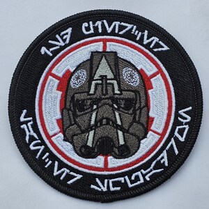 May include: A black and white embroidered patch with a red border. The patch features a stylized helmet with a white symbol and the text "117th  IV  V77  VCL77  IV" in Aurebesh.