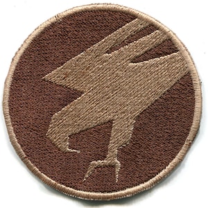 May include: A brown embroidered patch with a tan eagle silhouette. The eagle is facing left and has its wings spread. The patch is circular and has a white border.