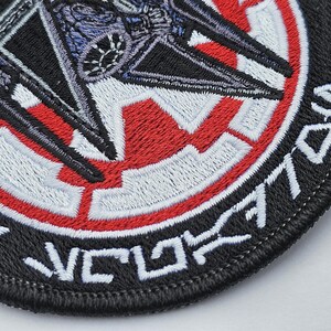 May include: Black and red embroidered patch with a white star in the center and a TIE fighter in the background. The text "TIE/vn" is embroidered around the edge of the patch.