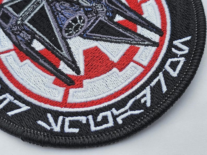 May include: Black and red embroidered patch with a white star in the center and a TIE fighter in the background. The text "TIE/vn" is embroidered around the edge of the patch.