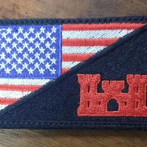 May include: A black and red embroidered patch with an American flag and a red fort design. The flag is folded diagonally with the stars facing the viewer. The fort is in the lower right corner of the patch.