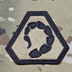 Op de afbeelding: Een geborduurde patch in tan en zwart met een schorpioenontwerp. De schorpioen is opgerold in een cirkel en is zwart omrand.