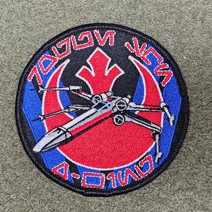 May include: A black, blue and red embroidered patch with the text "TOGOWAN VCS" and "D-01W107" around a red and blue Rebel Alliance symbol with a white X-wing fighter in the centre.