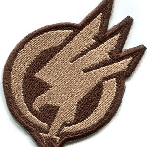 May include: A brown and tan embroidered patch with a stylized eagle design. The eagle is facing right and has its wings spread. The eagle is surrounded by a circle.
