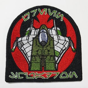 Könnte beinhalten: Ein gestickter Patch in Schwarz, Rot und Grün mit einem Star Wars Rebellenallianz-Symbol und einem Sternenjäger in der Mitte. Der Text "V-4X-D" und "777" befindet sich auf dem Patch.