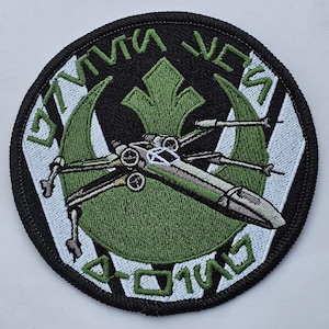 Puede incluir: Un parche bordado verde y blanco con un caza X-wing de Star Wars y el texto "STAR WARS" y "ROGUE SQUADRON".